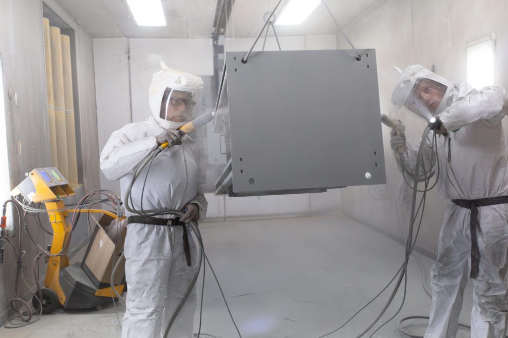 two men dressed in protective gear powder coating metal part