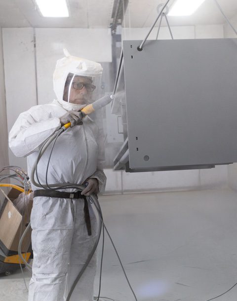man wearing protective gear completing powder coating on metal part