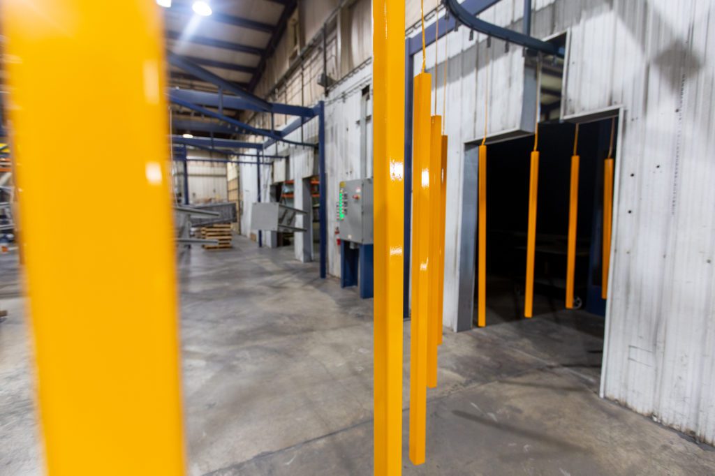 Bright orange powder coated parts travel on a conveyor.