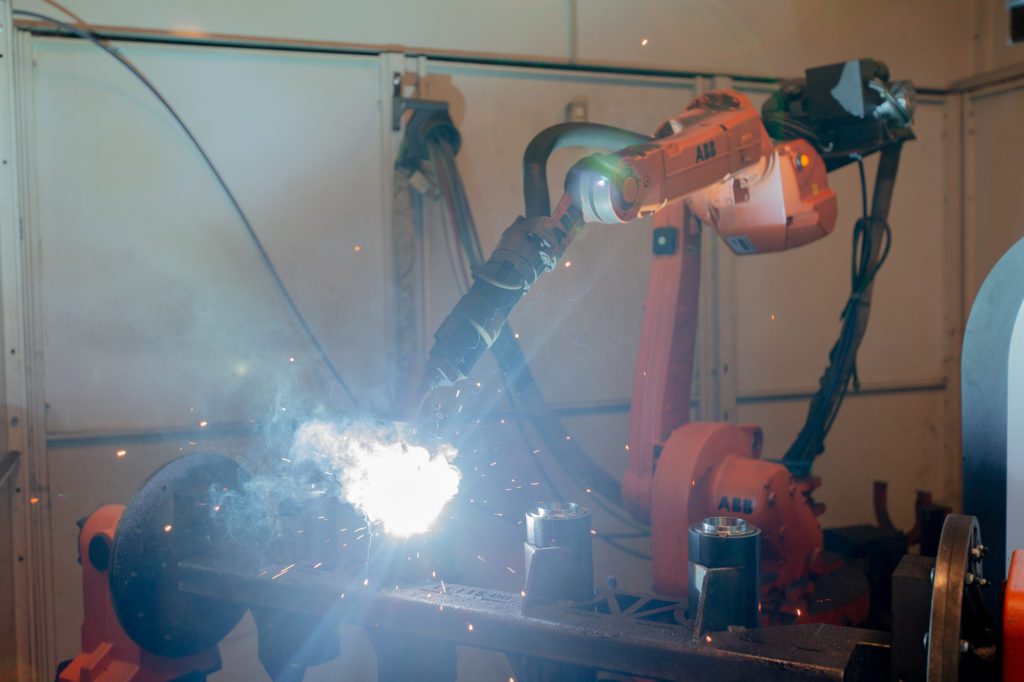A robotic arm welds a metal part at Metaltech.