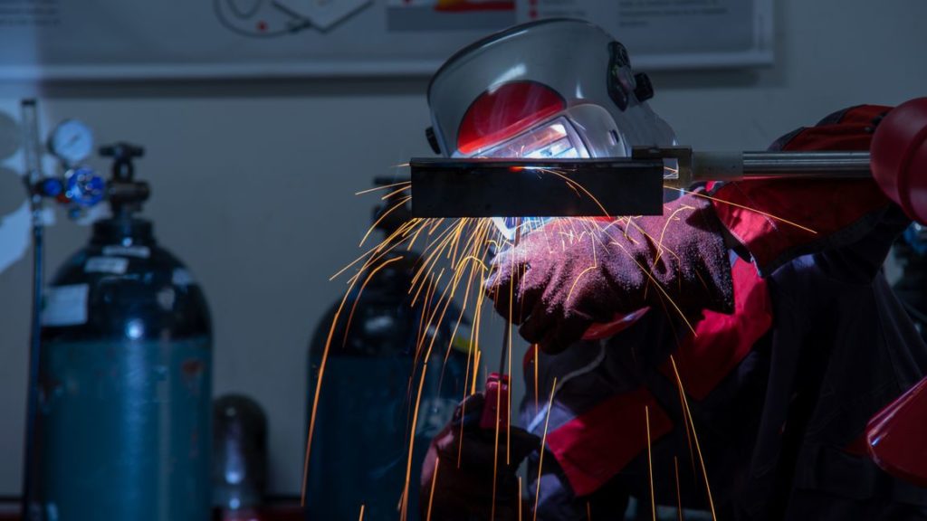 Professional welder MIG welding a stainless steel pipe with a torch and shielding gas.