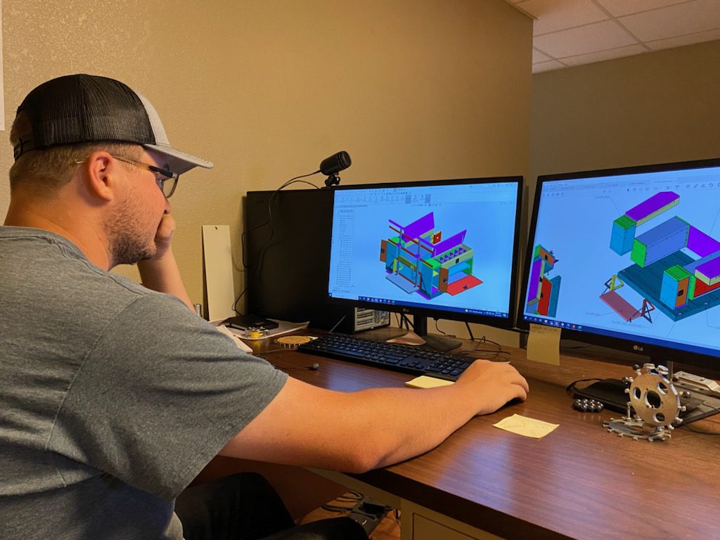 Engineer sits at computer, testing solid models of metal components for a customer.