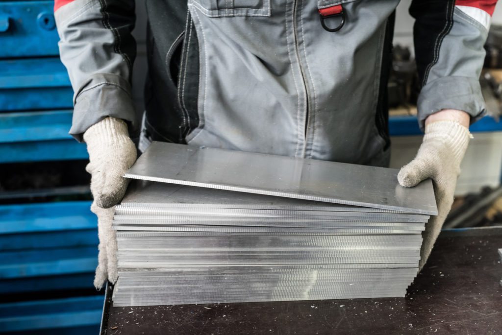 A person handles a stack of sheet metal cut down to size.