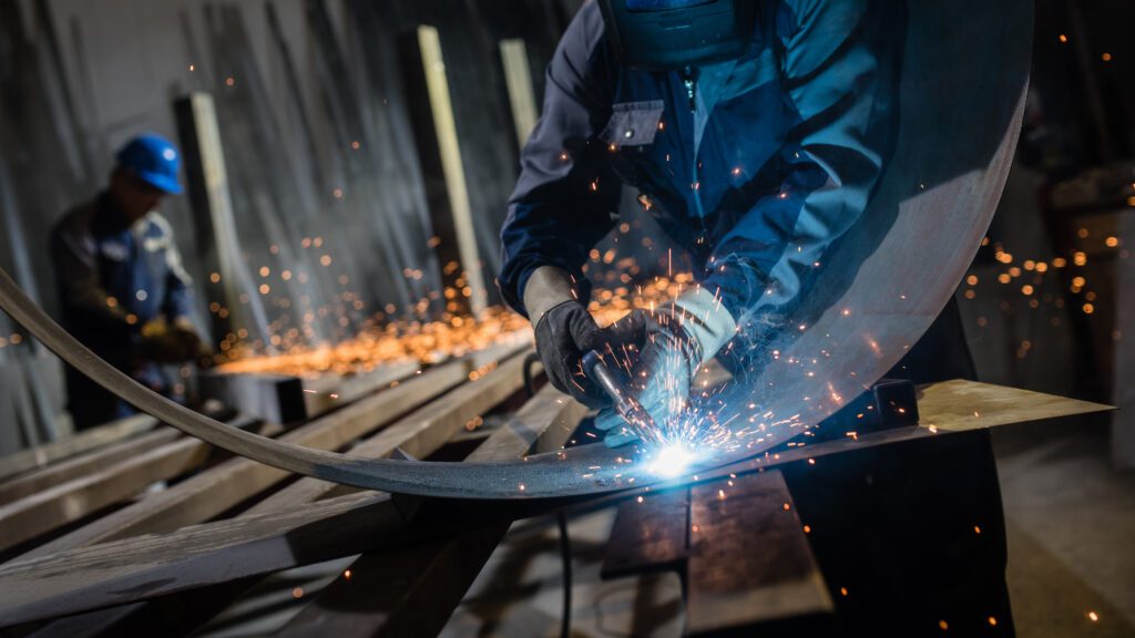 Worker using welding torch to cut metal sheet in workshop.